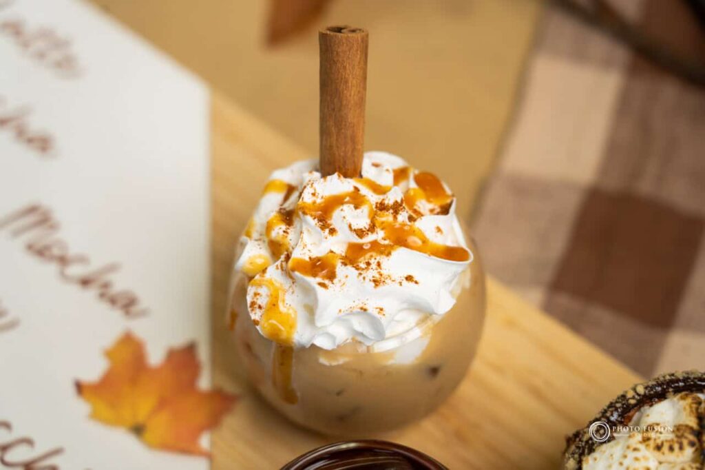 This is an image of the cinnamon carmel coffee from the coffee flight at Jojo's Coffeehouse Breakfast & Brunch. This image was taken for the fall menu and has a cinamon stick poking out of the top. There is also whip cream on the top of the drink with carmel and cinamon on top of the whip cream.