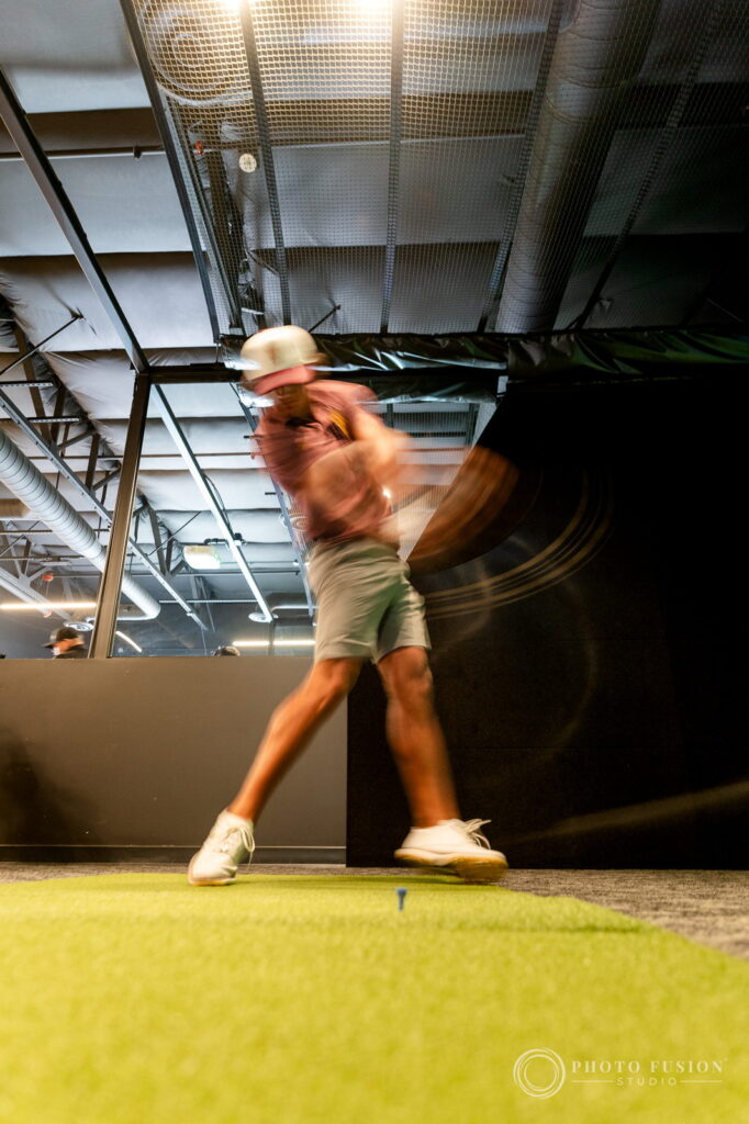 A motion-blurred low angle frame of an ASU golfer swinging through impact on the hitting mat