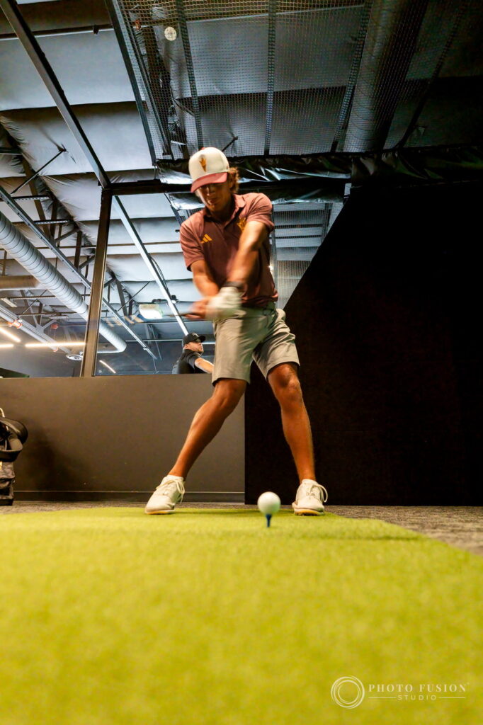Low angle view of an ASU men's golf player mid-swing over a teed ball on the hitting mat