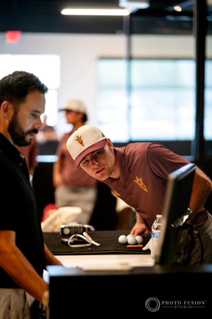 An ASU golfer leans over a monitor to study his fitting numbers alongside a True Spec fitter