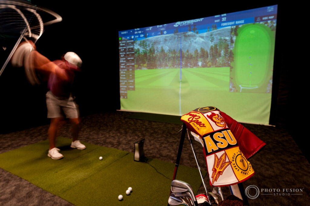 An ASU golfer's swing blurs across a fitting bay while a maroon and gold ASU headcover sits in focus
