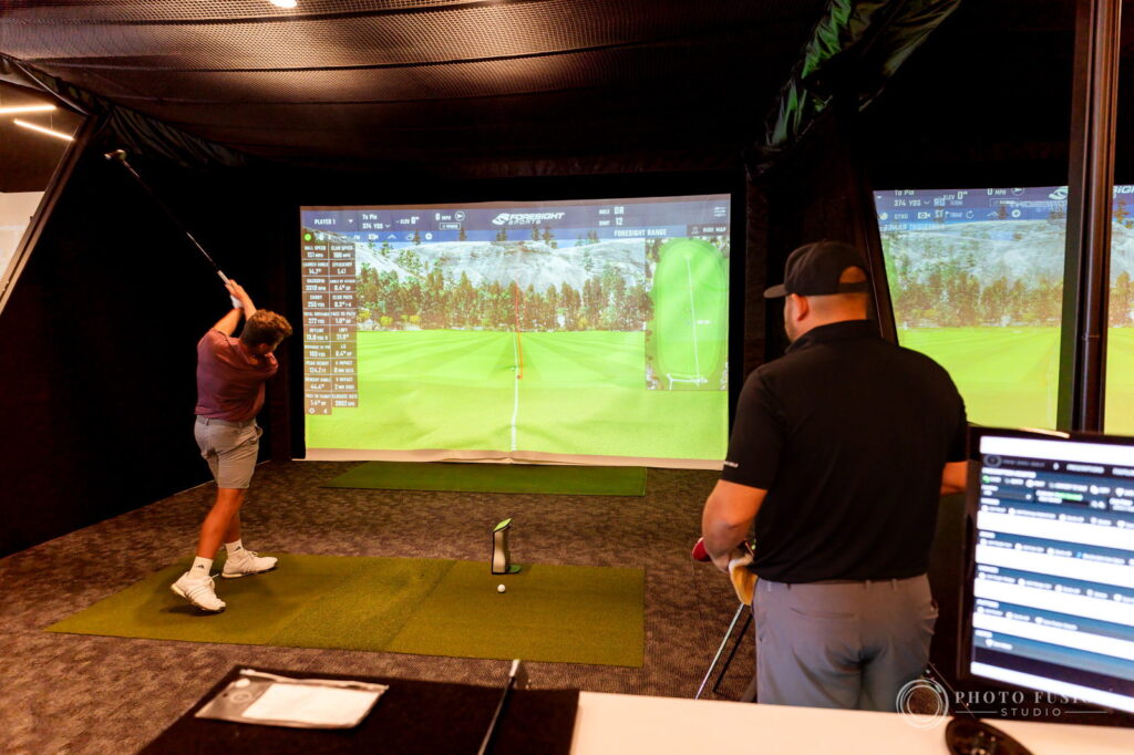 An ASU golfer at the top of his backswing while a True Spec fitter watches the launch monitor readout