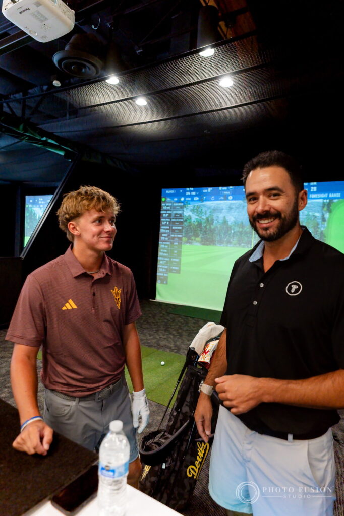 An ASU golfer and a True Spec Golf fitter smile beside a bag as simulator screens glow behind them