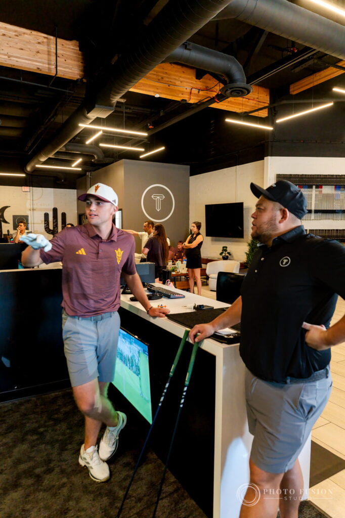 An ASU golfer walks across the True Spec Golf showroom carrying a club beside a fitter holding shafts