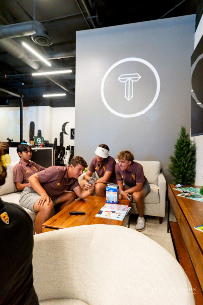 Four ASU men's golf players sit on a couch looking at a phone under the True Spec Golf logo