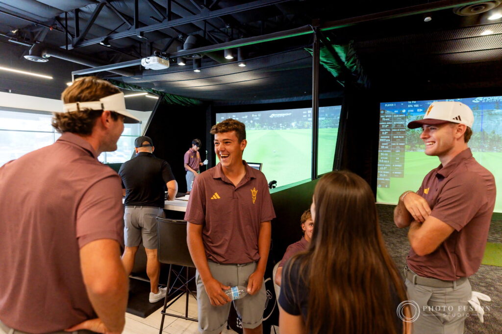 A group of ASU men's golf players laugh together in the True Spec Golf fitting studio between sessions