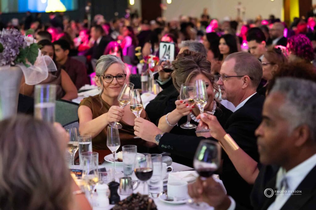 This is a photo taken at the AZHCC annual black and white ball and business awards. This is an image of a toast where everyone is cheersing, you can see Arizona Governor Katie Hobbs clicking glasses with people at the table.