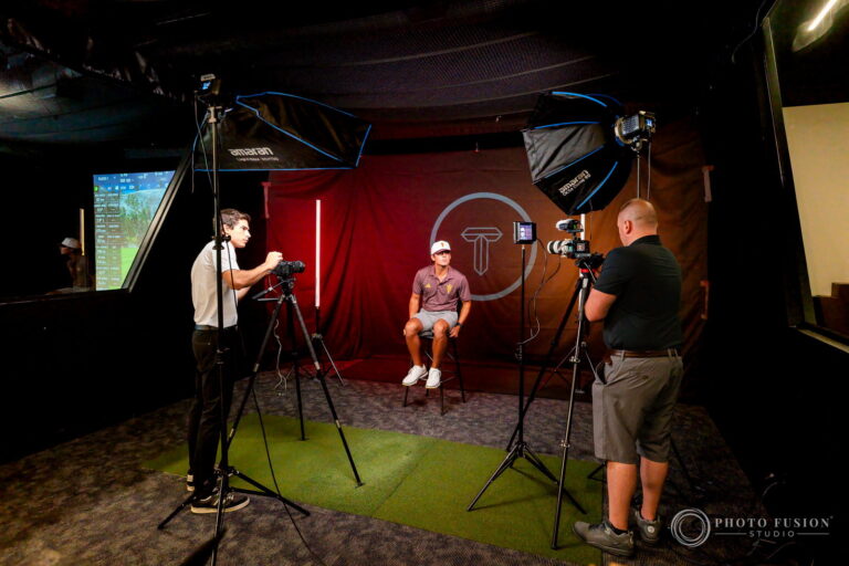 A wide behind the scenes view of a two-camera interview setup with softboxes at True Spec Golf