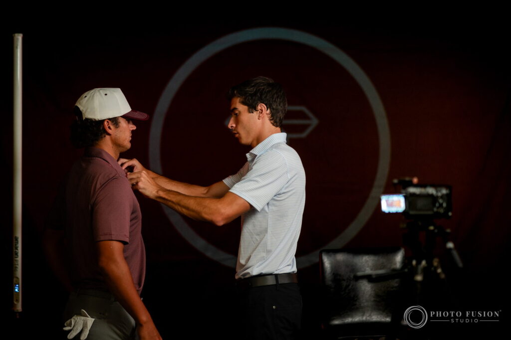 A crew member clips a lavalier microphone onto an ASU golfer's polo before an on-camera interview