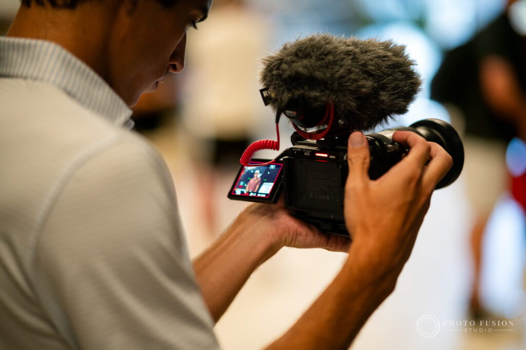 A videographer reviews footage on a mirrorless camera with a shotgun microphone mounted on top
