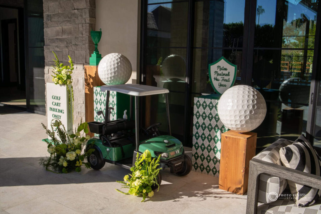 Golf cart for a young child surrounded by floral decor and giant golf balls. There is a sign that says golf cart parking only and another that says mateo mastered his first year.