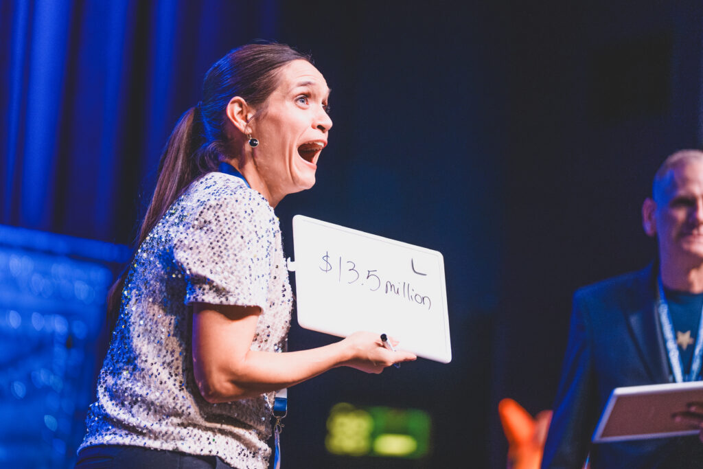 A guest reacts while holding a whiteboard reading $13.5 million during a prize game at the Chandler Chamber Community Awards