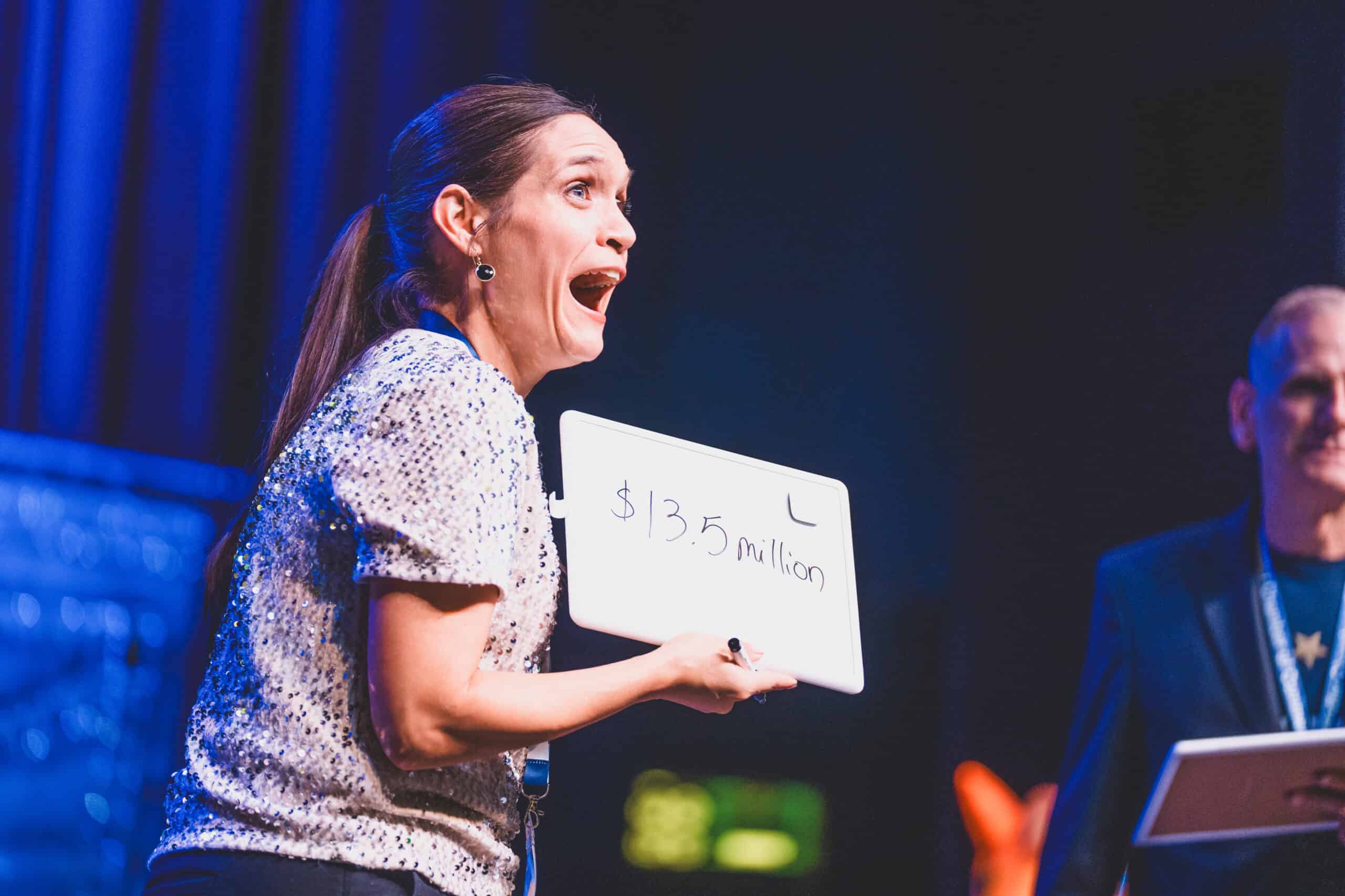 A guest reacts while holding a whiteboard reading $13.5 million during a prize game at the Chandler Chamber Community Awards