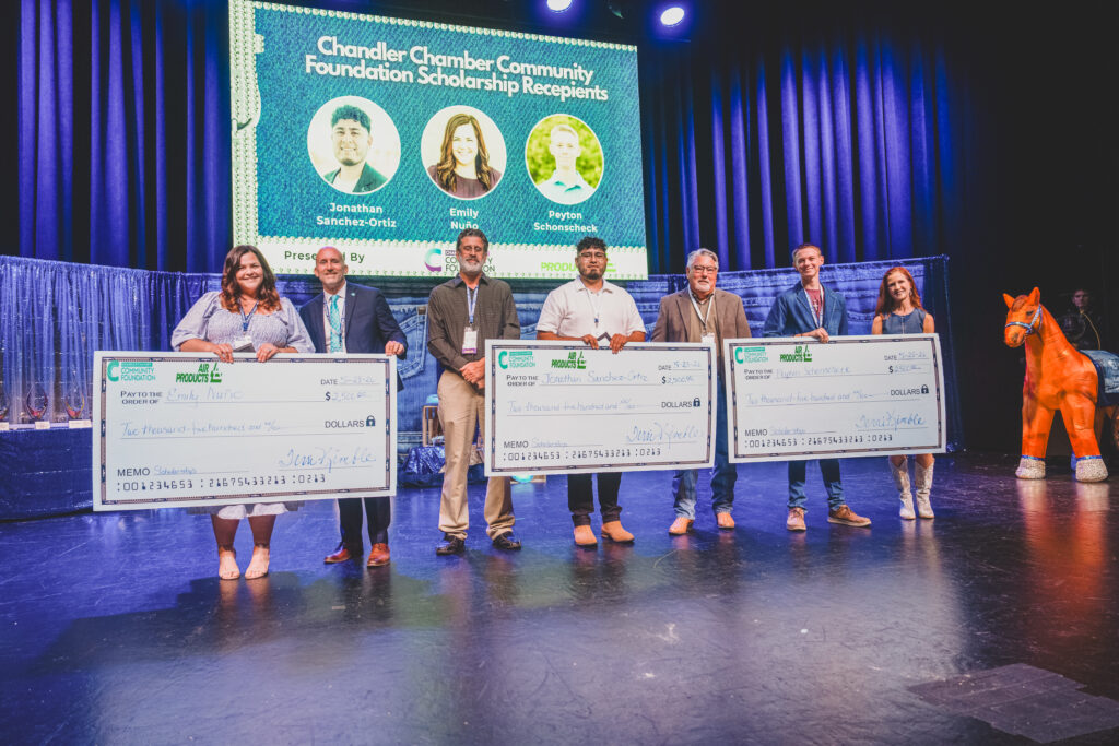 Scholarship recipients Jonathan Sanchez-Ortiz, Emily Nuno, and Peyton Schonscheck hold oversized checks on stage