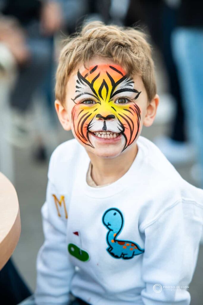 This is a photo of a child with tiger face paint. He is at a one year olds birthday party.