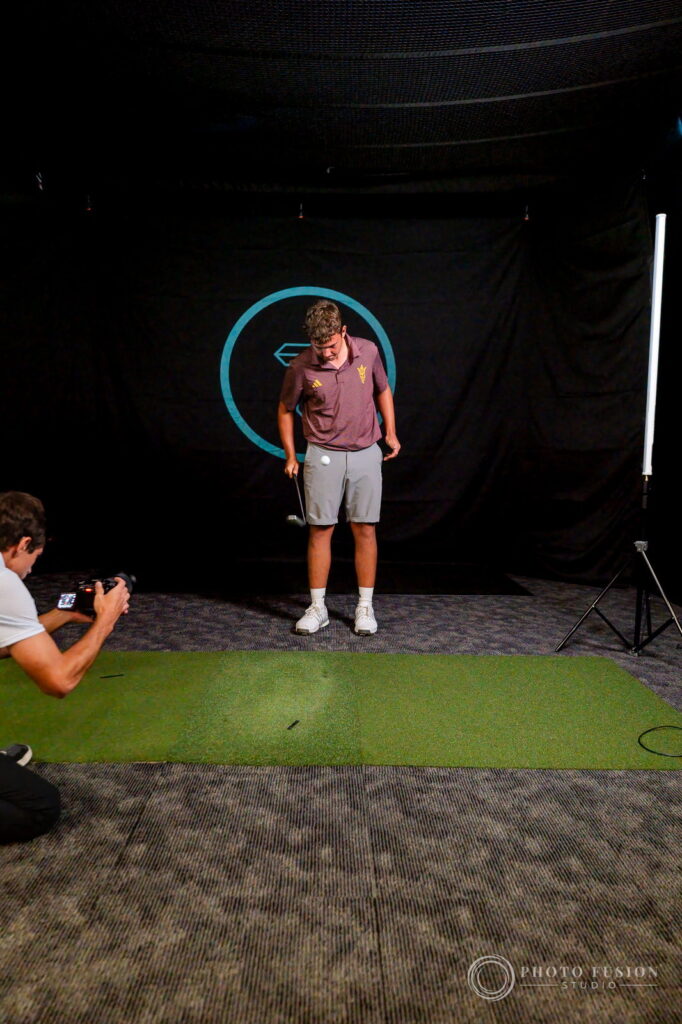 A golf photographer kneels on the mat to shoot an ASU player at True Spec Golf Scottsdale