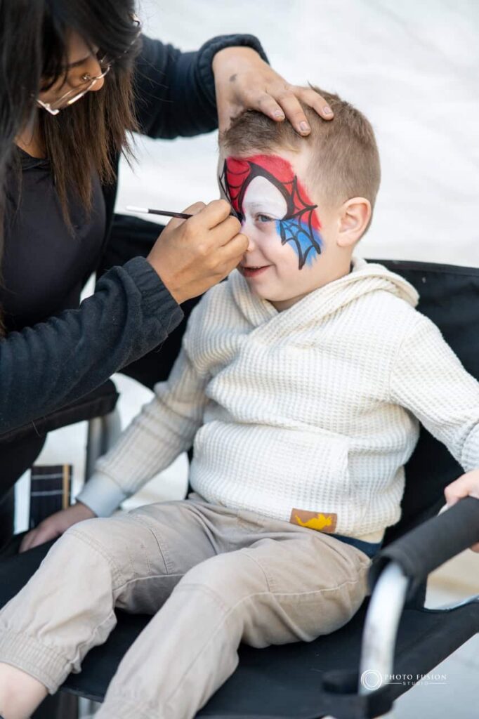 Child in a face painting chair getting his face painted at a one year olds birthday party. He is getting a spiderman design on his face.
