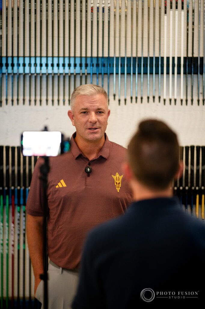 ASU head coach Matt Thurmond speaks to a phone camera in front of a full wall of colored golf shafts