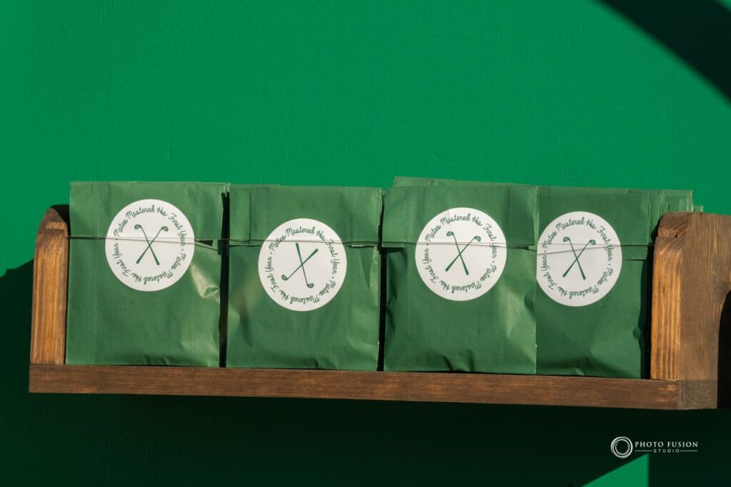 Up close shot of snacks that are on a shelf hanging on a wall. They are in green packaging and the sticker has two golf clubs in the center, the words around it say mateo mastered his first year.