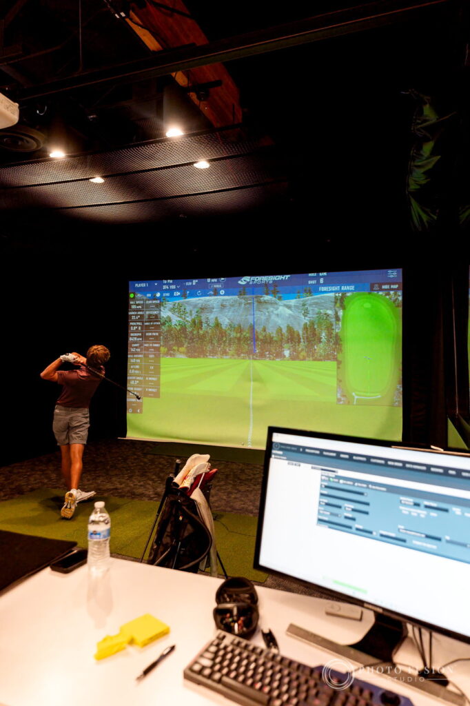 An ASU golfer swings toward a Foresight simulator screen while GCQuad fitting data fills a nearby monitor