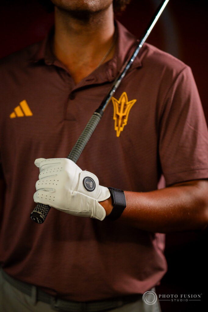Close-up of a gloved hand holding a golf club against an ASU maroon polo with a gold pitchfork logo