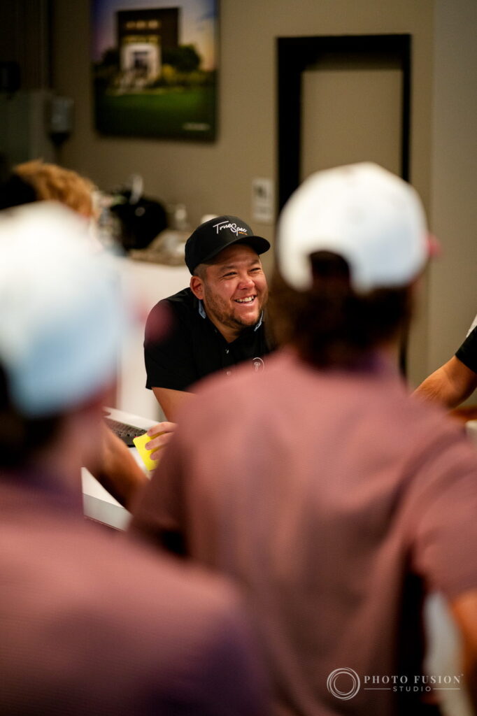 A True Spec Golf staff member in a branded cap laughs with ASU golfers gathered around the fitting counter