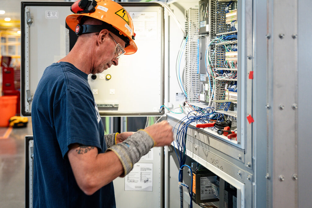 XNRGY technician in a hard hat wiring an electrical control panel inside a finished cooling unit at the Mesa Gateway facility.