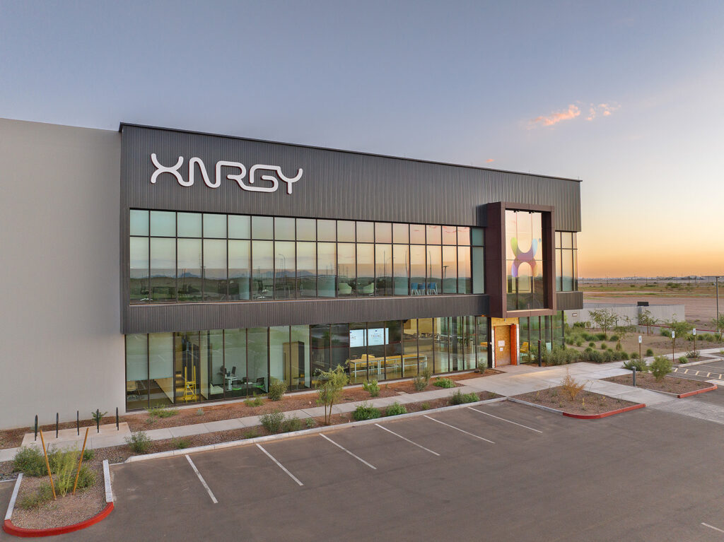 Corporate video production Phoenix shoot at XNRGY facility Mesa Gateway. Aerial sunrise view of XNRGY's main entrance with illuminated logo and colorful X art installation near Mesa Gateway Airport.