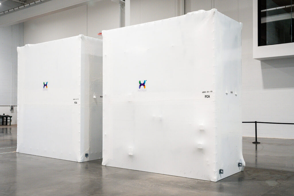 Two large XNRGY cooling units shrink-wrapped in white protective covers staged for shipment at the Mesa Gateway facility.