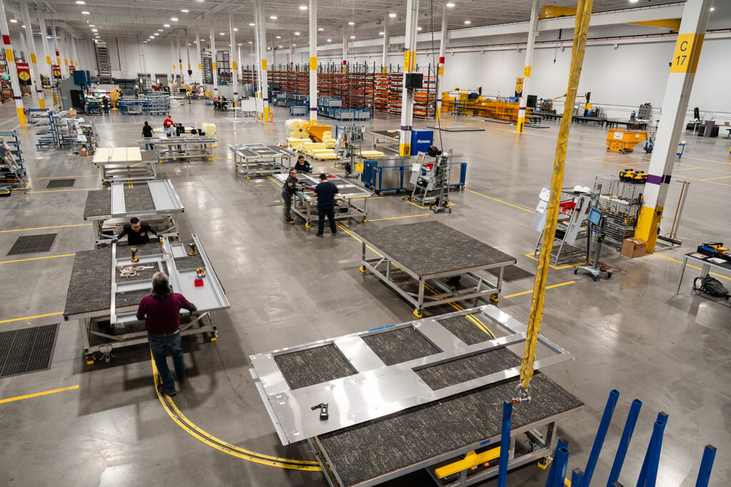 Elevated wide view of multiple XNRGY frame assembly stations with workers building large metal frames at the Mesa Gateway facility.