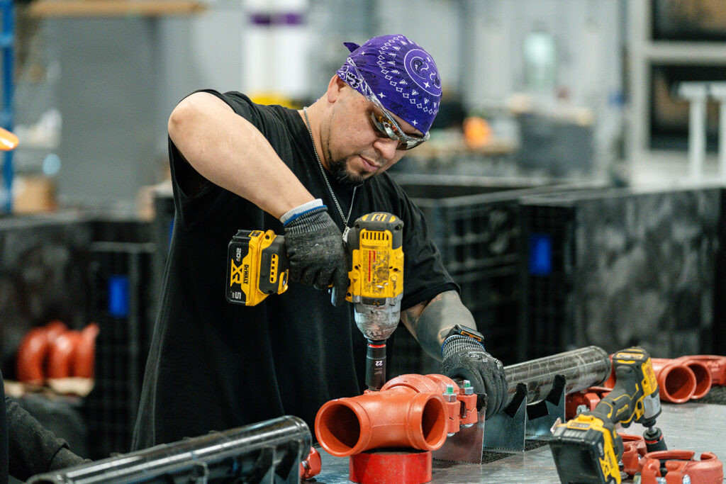 XNRGY worker using an impact driver to assemble red grooved piping fittings at the Mesa Gateway facility.