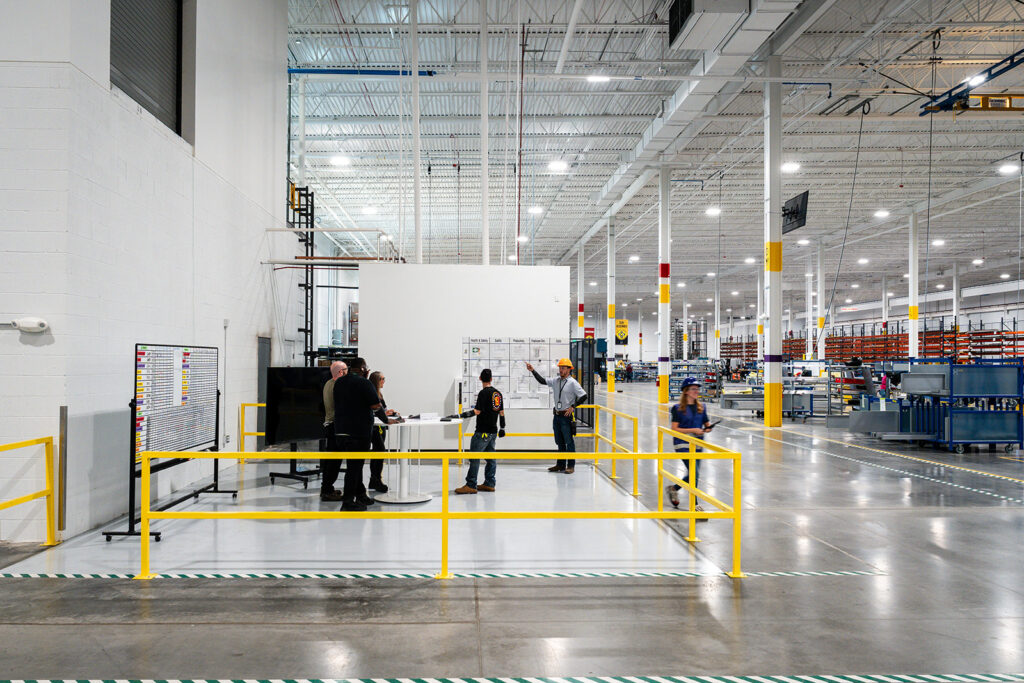 Wide interior view of the XNRGY production floor with team members gathered around a production information board at the Mesa Gateway facility.