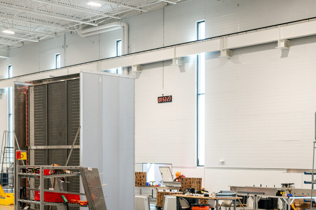 XNRGY production area with a digital takt-time timer mounted overhead and assembly workstations inside the Mesa Gateway facility.
