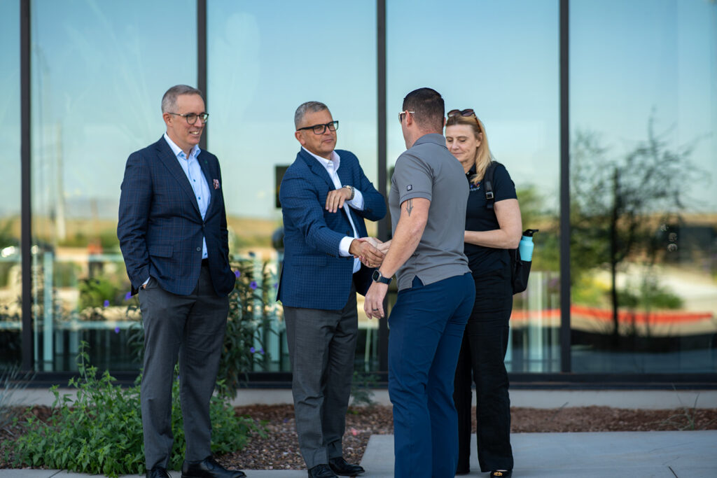 XNRGY leadership greeting arriving guests with a handshake outside the glass facade of the Mesa Gateway facility during the ribbon cutting welcome reception.