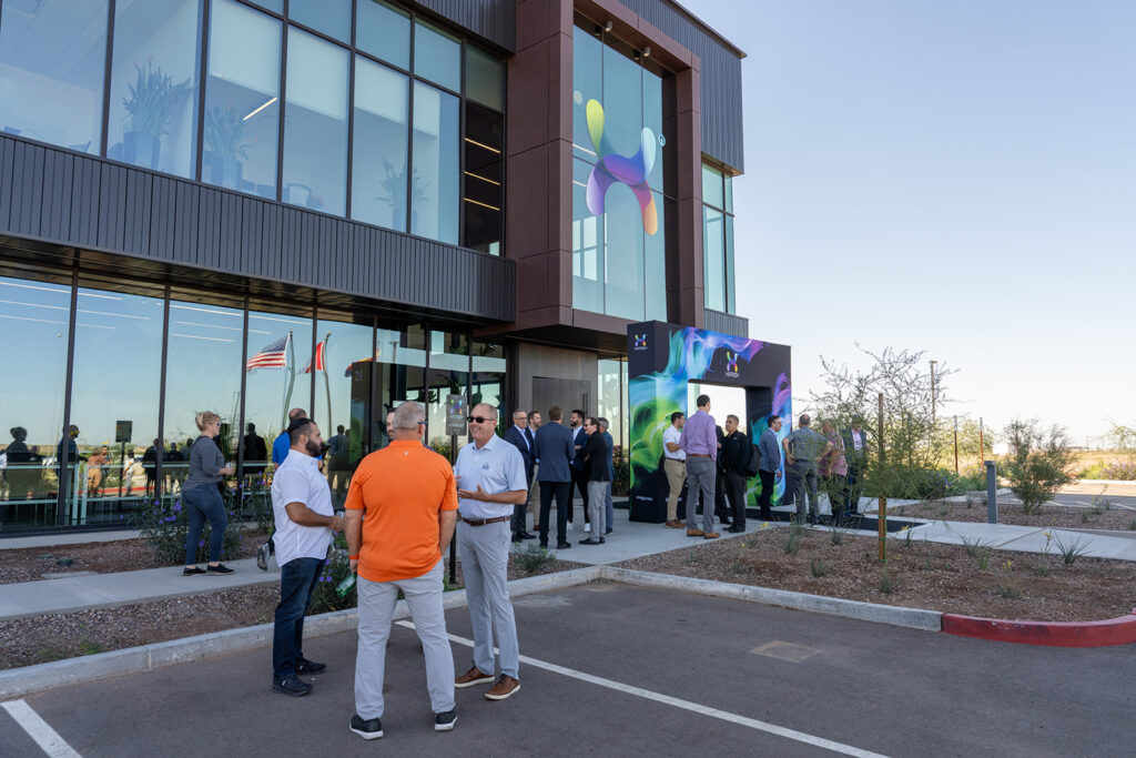 Guests gathering at the front entrance of the XNRGY Mesa Gateway facility near a large digital X art display during the ribbon cutting welcome reception.