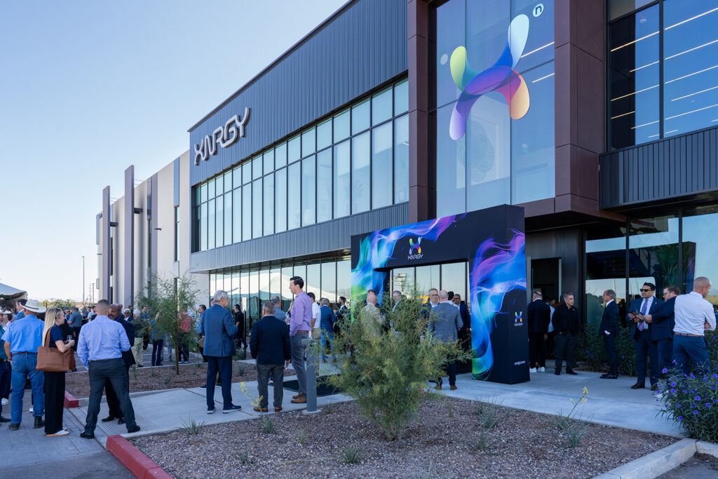 Wide view of the XNRGY Mesa Gateway facility entrance with attendees gathered around the large digital X art display during the ribbon cutting welcome reception.