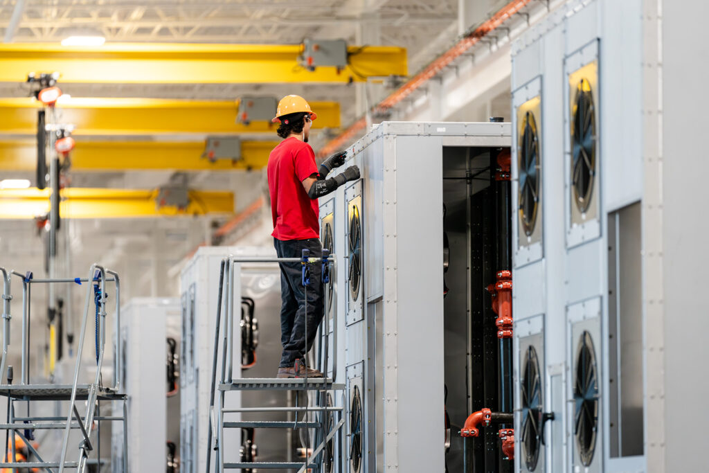 XNRGY technician on a platform working on the top of a large cooling unit cabinet with a fan array at the Mesa Gateway facility.