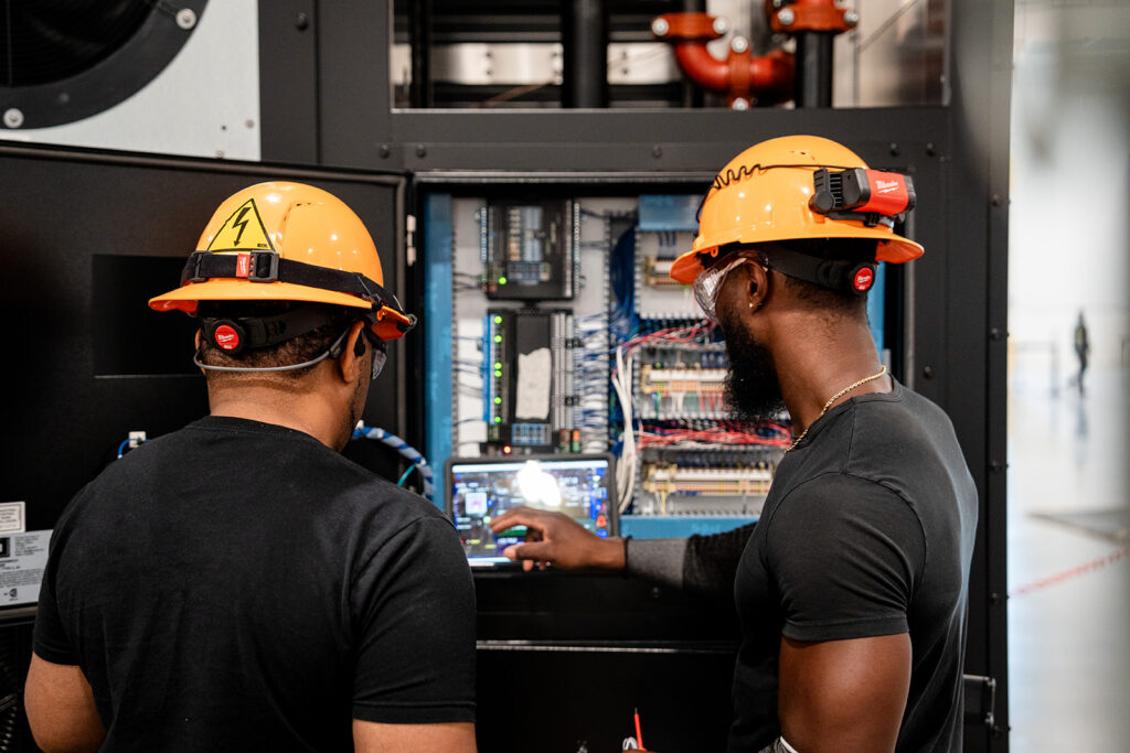 Two XNRGY technicians in hard hats commissioning a control panel inside a data center cooling unit at the Mesa Gateway facility.