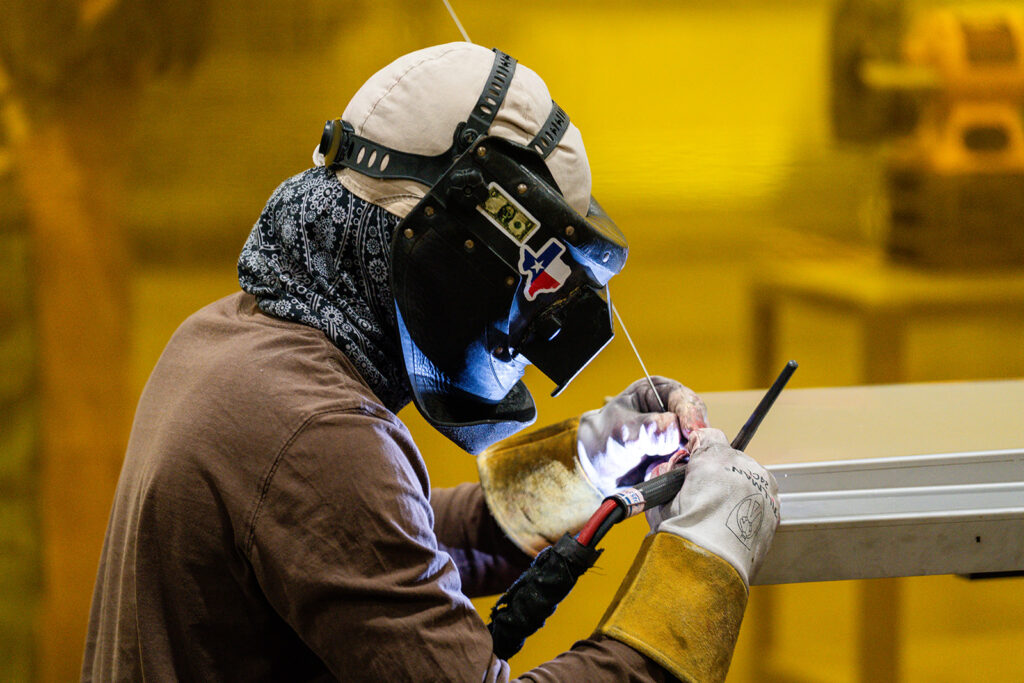 XNRGY welder in protective hood TIG welding metal stock at the Mesa Gateway facility.