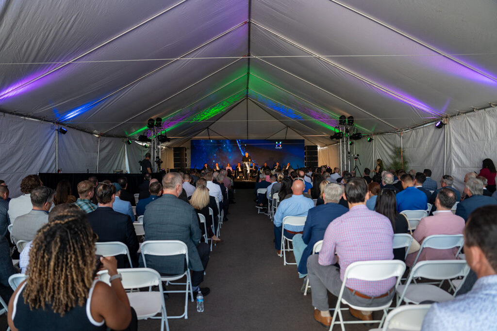 Wide view of the seated audience under a white event tent facing the stage during the XNRGY ribbon cutting ceremony at the Mesa Gateway facility.