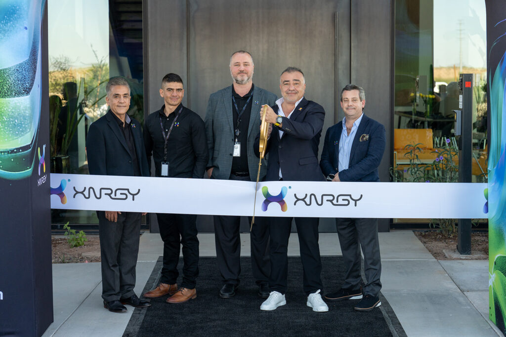 XNRGY CEO Wais Jalali with company leaders in a posed portrait behind the ceremonial ribbon at the Mesa Gateway facility entrance.