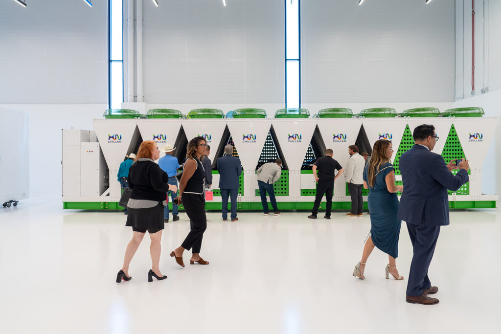 Ribbon cutting guests viewing the XNRGY XnChiller product lineup in green and white in the display hall at the Mesa Gateway facility.